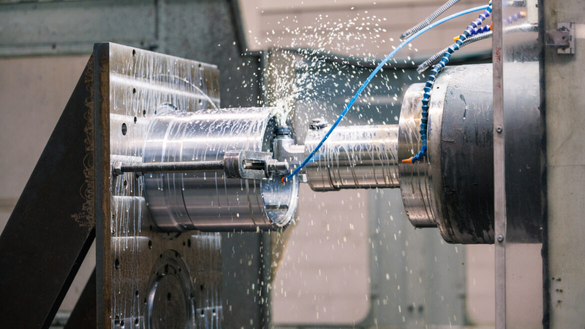 een grote CNC-bewerkte hydraulische cilinder of industriële as die wordt verspaand in een CNC-kotterbank of draaibank, terwijl er koelvloeistof wordt gebruikt om hitte en wrijving te verminderen